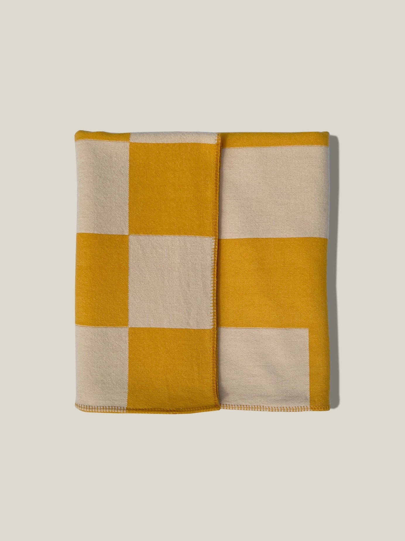 Aspen Throw Blanket in mustard color shown folded with square pattern on white background