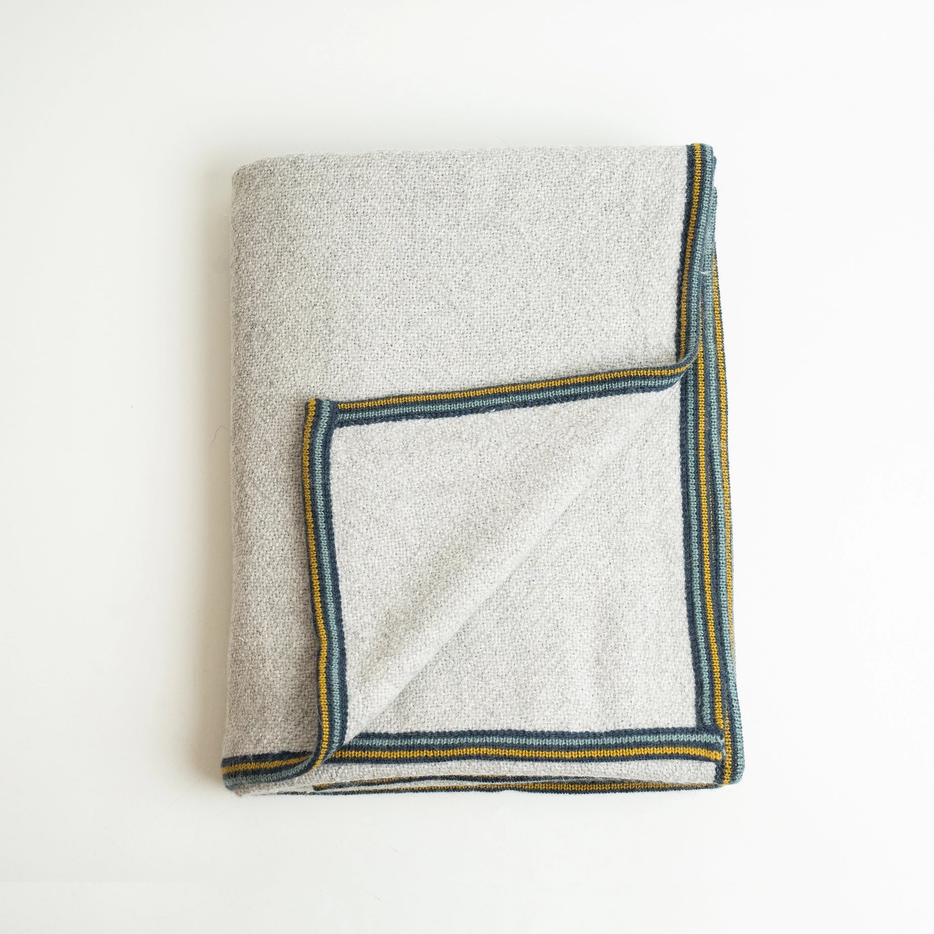 Alpaca wool blanket in gray with striped border, shown folded with corner flipped up on white background