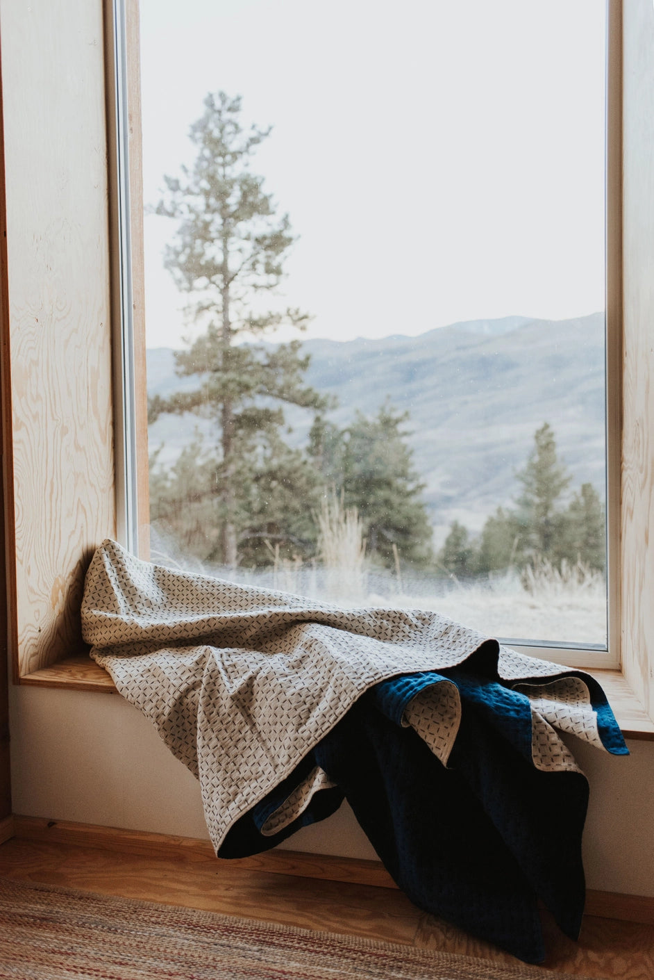 Handmade blanket by Happy French Gang, in indigo and natural color shown on modern wood window sill with nature view