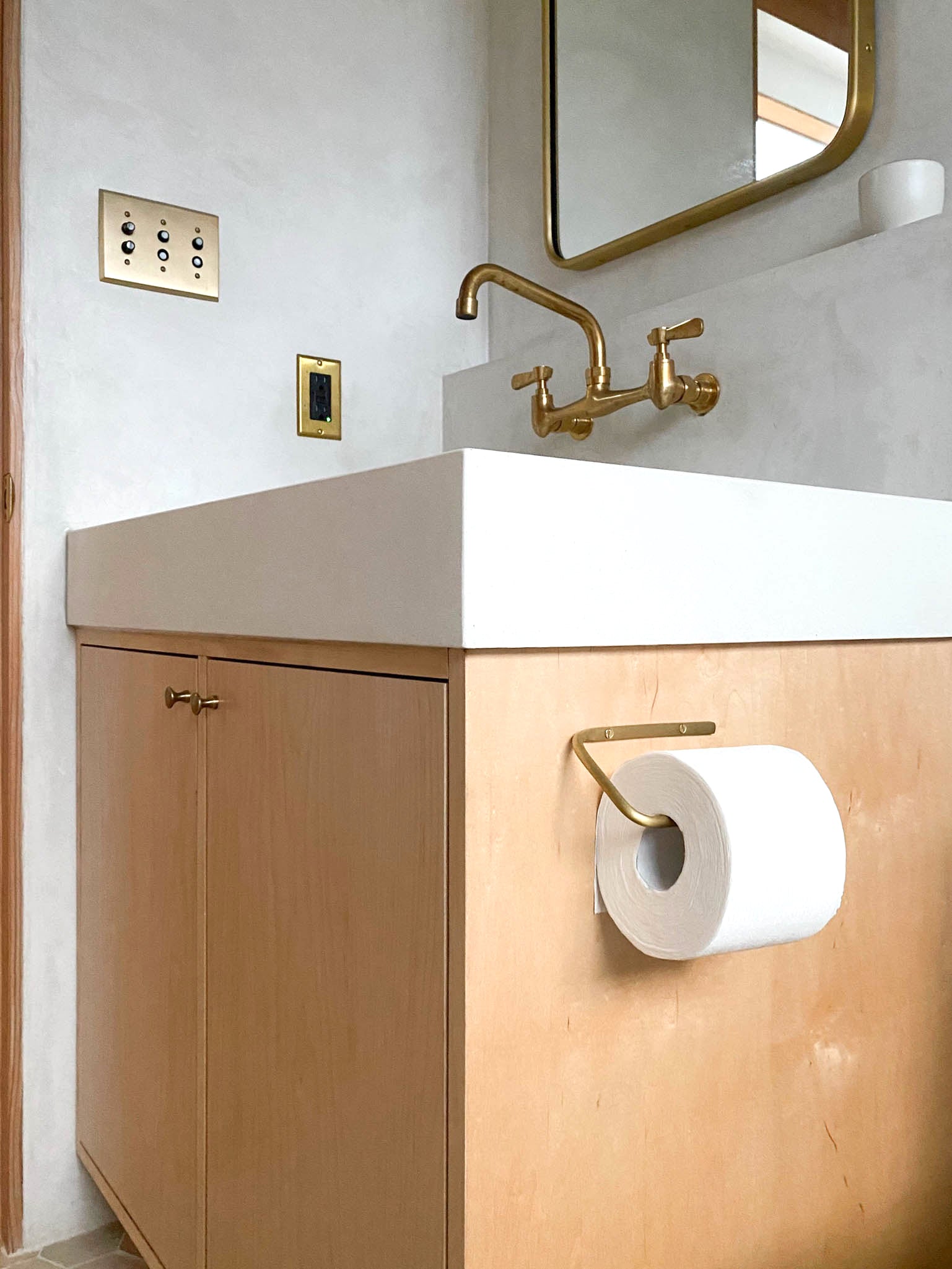 Fog Linen Brass Toilet Paper Holder shown on side of cabinet in bathroom