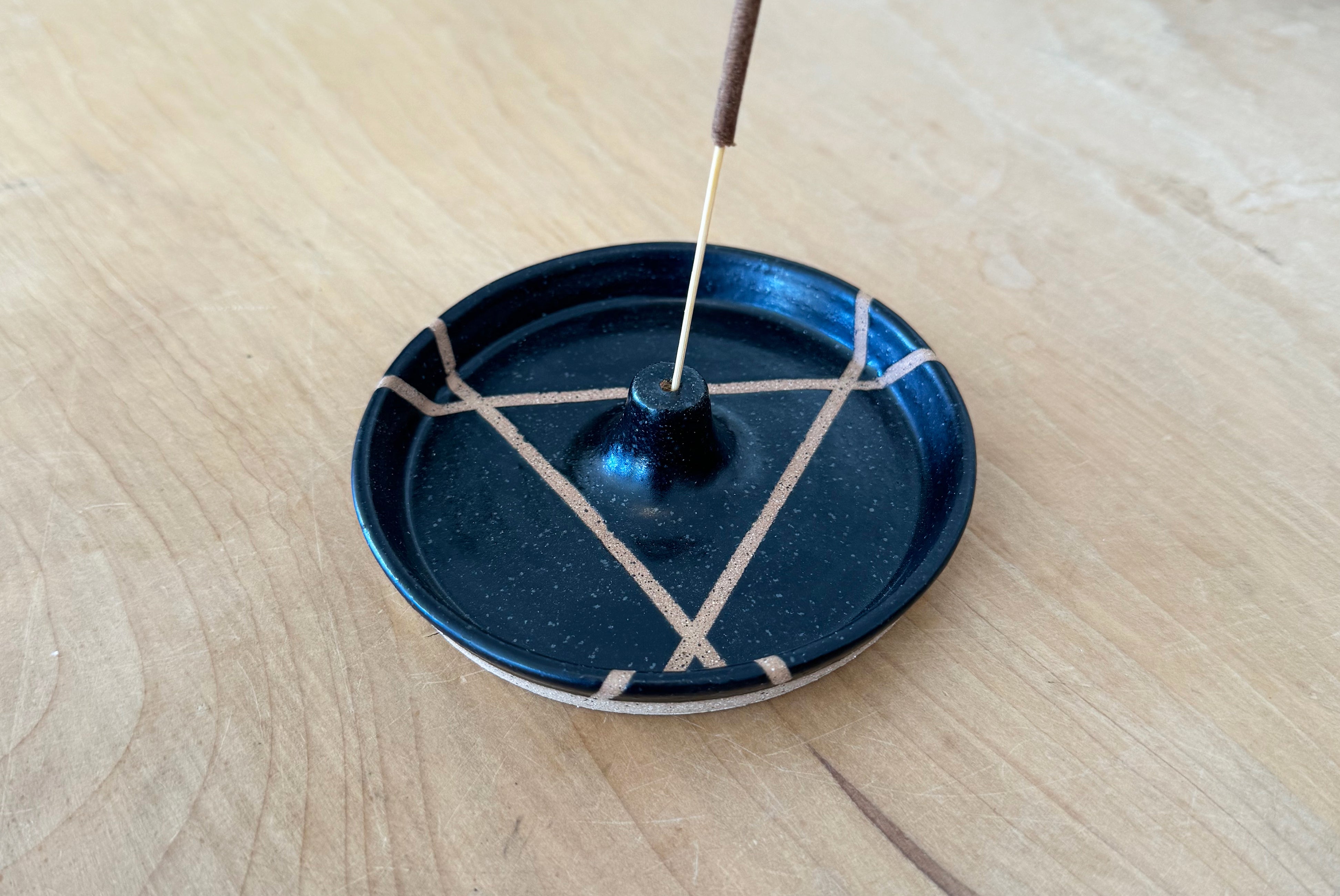 Close up view of Ceramic Incense Holder by Fred James Pottery in matte black, shown with incense on wood surface