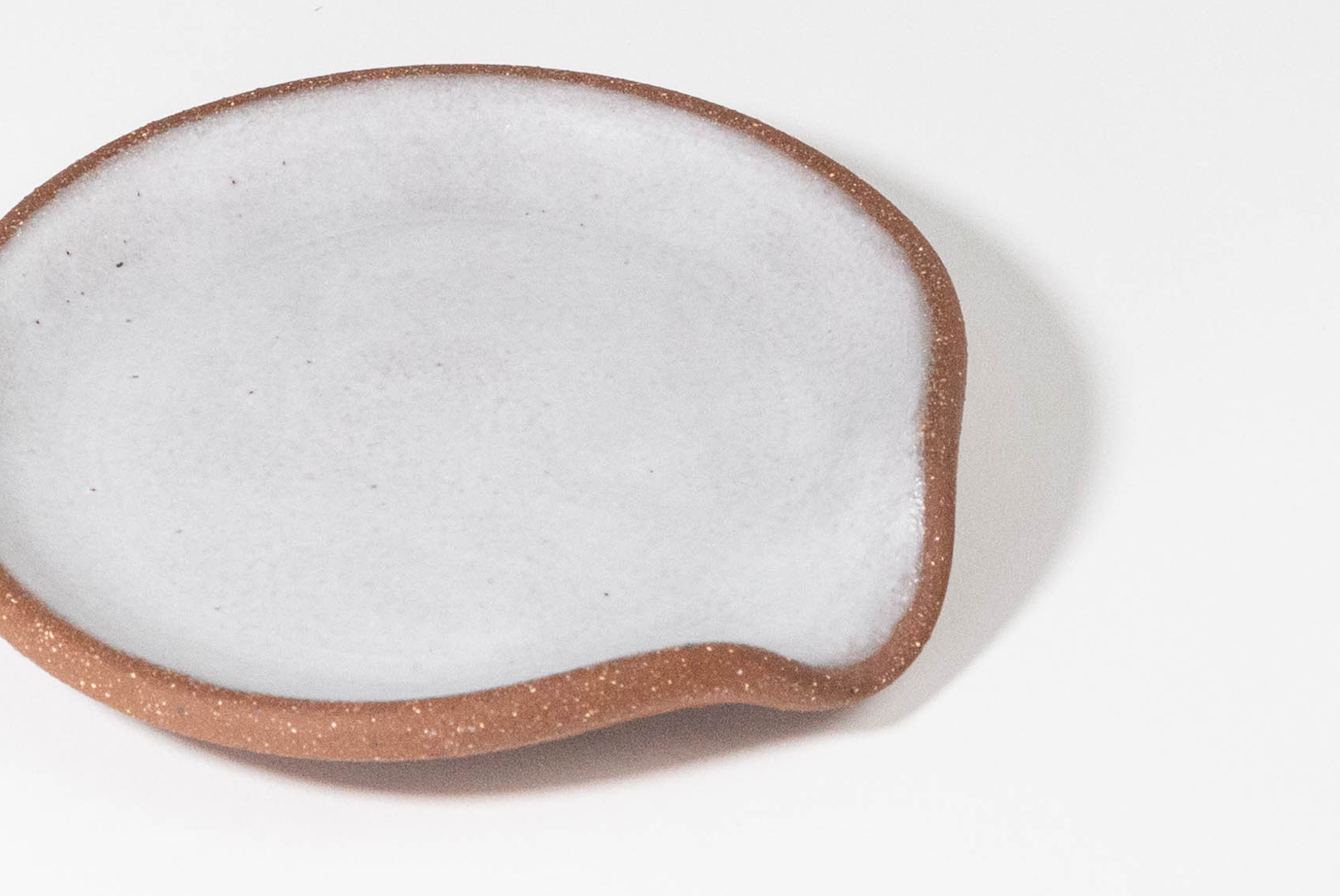 Close up of Ceramic Spoon Rest by Fred James Pottery in textured brown clay and matte white glaze, shown on white background