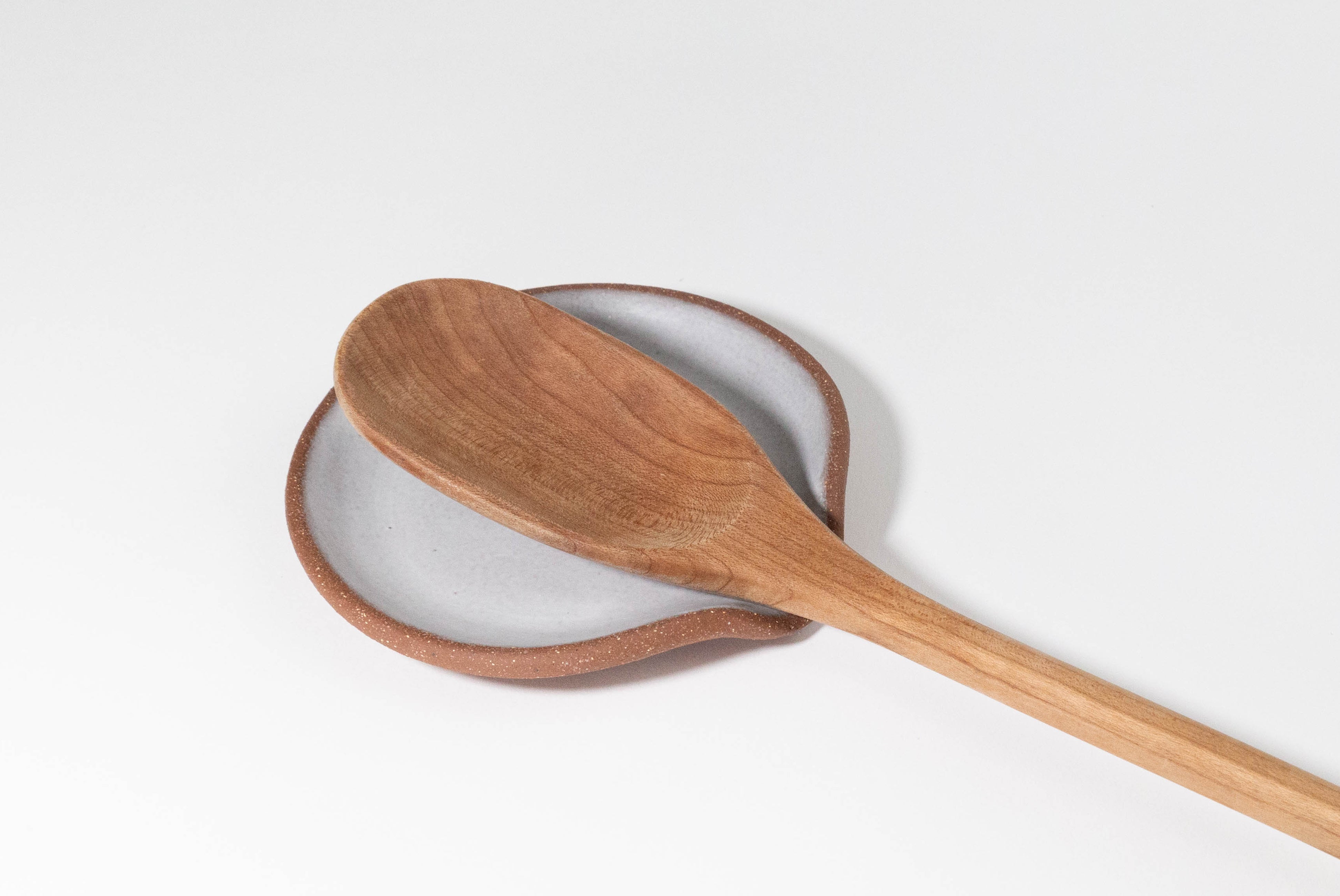 Ceramic Spoon Rest by Fred James Pottery in textured brown clay and matte white glaze, shown with wooden spoon on white background