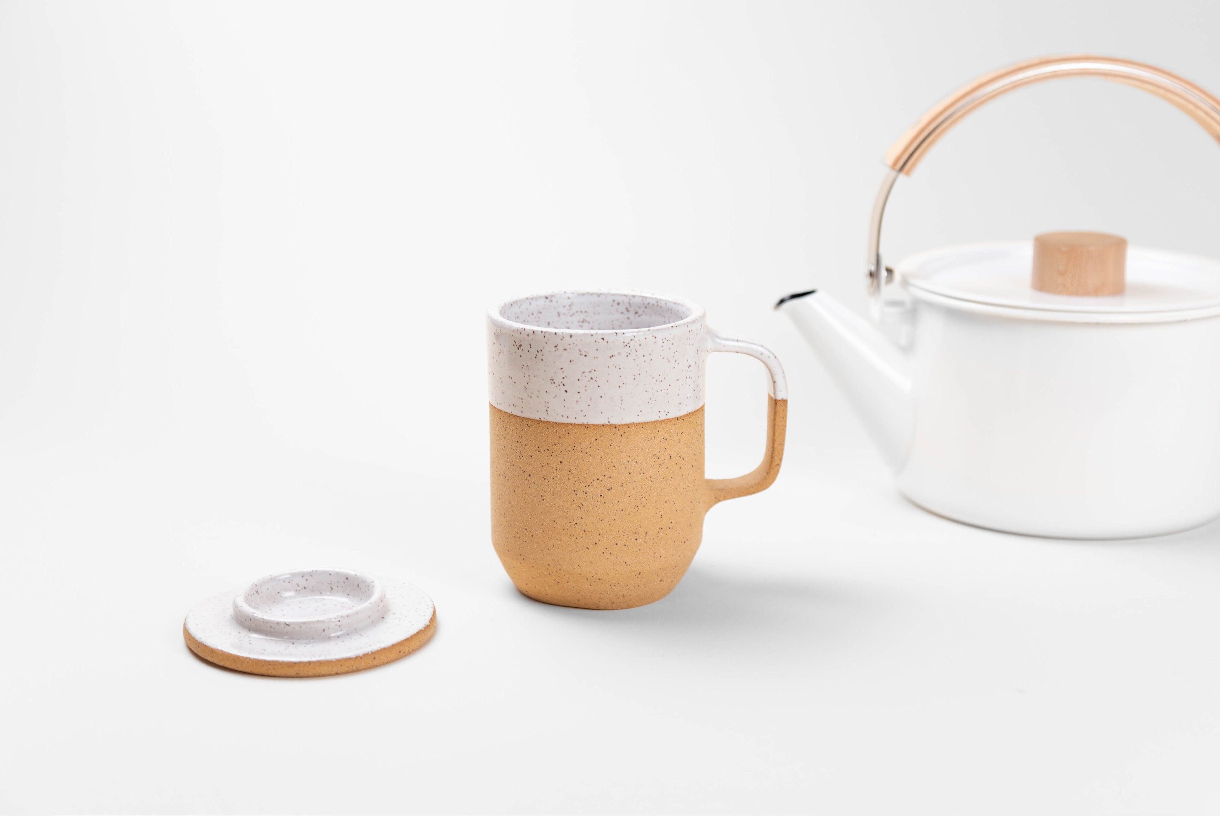 Ceramic Tea Mug with Lid in natural textured clay with speckled matte white glaze on top half, shown with lid being used to place tea bag, on white background with white Japanese kettle