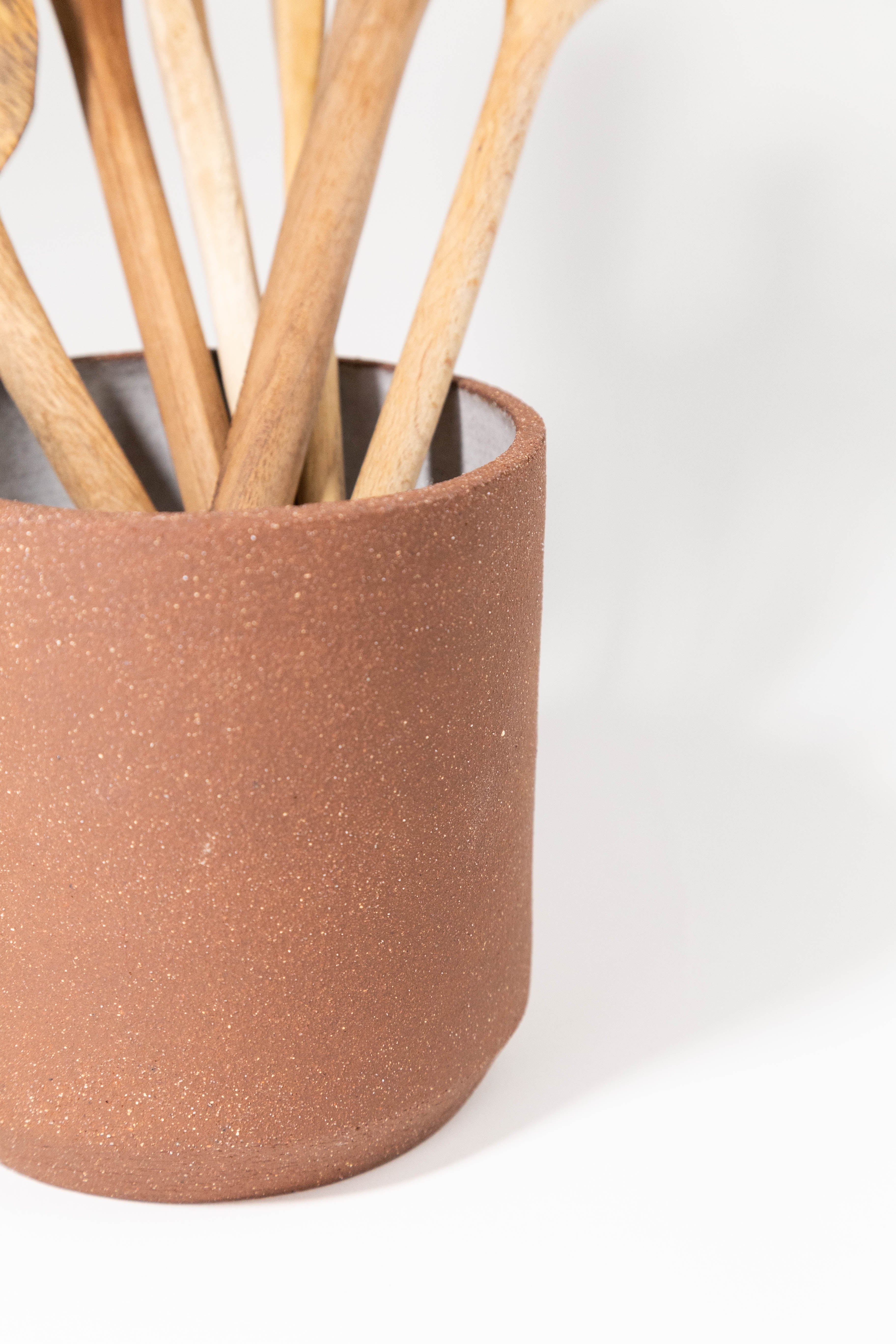 Close up of Ceramic Utensil Holder by Fred James Pottery shown with wooden utensils on white background
