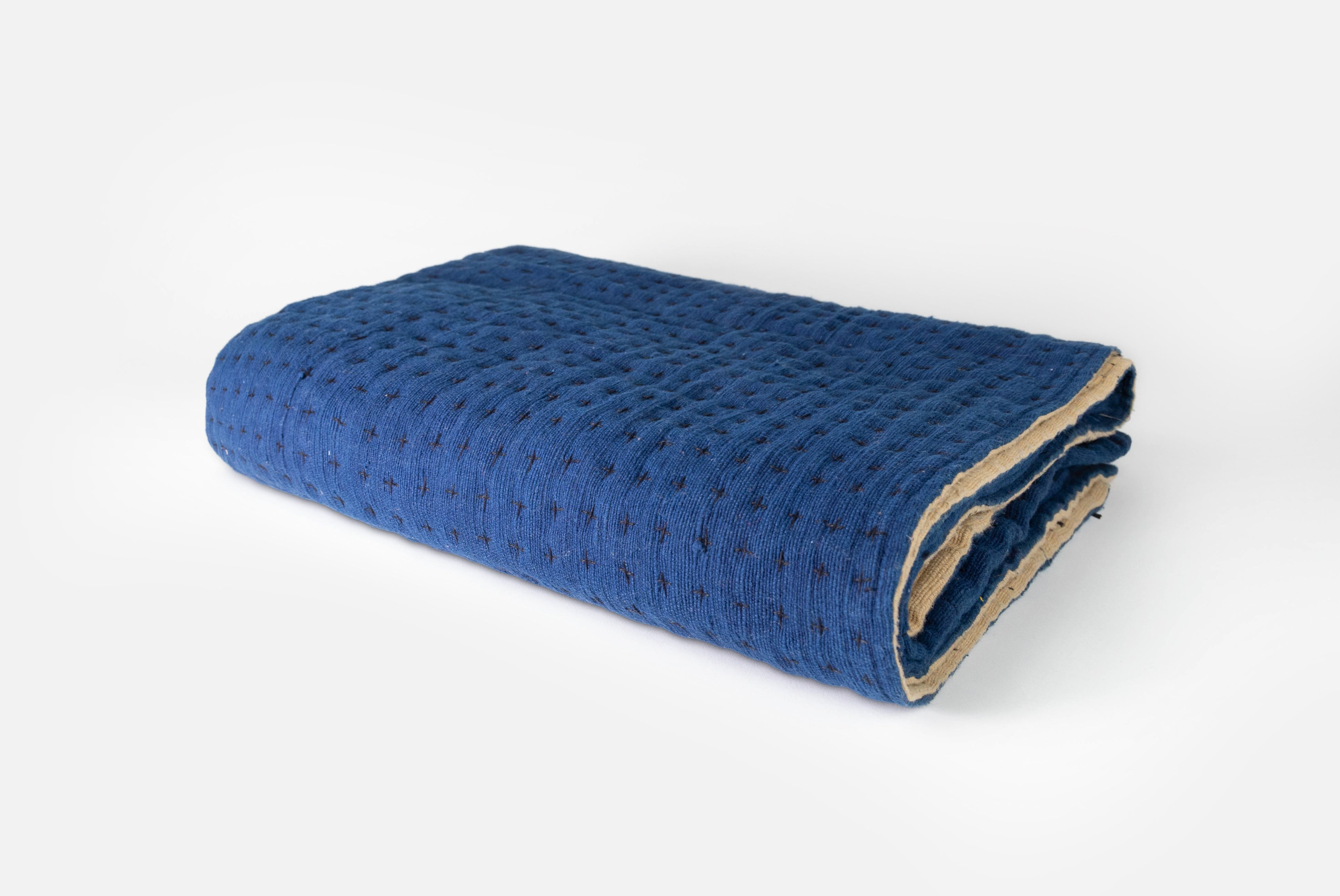 Handmade blanket by Happy French Gang, shown folded in indigo and natural color, on white background