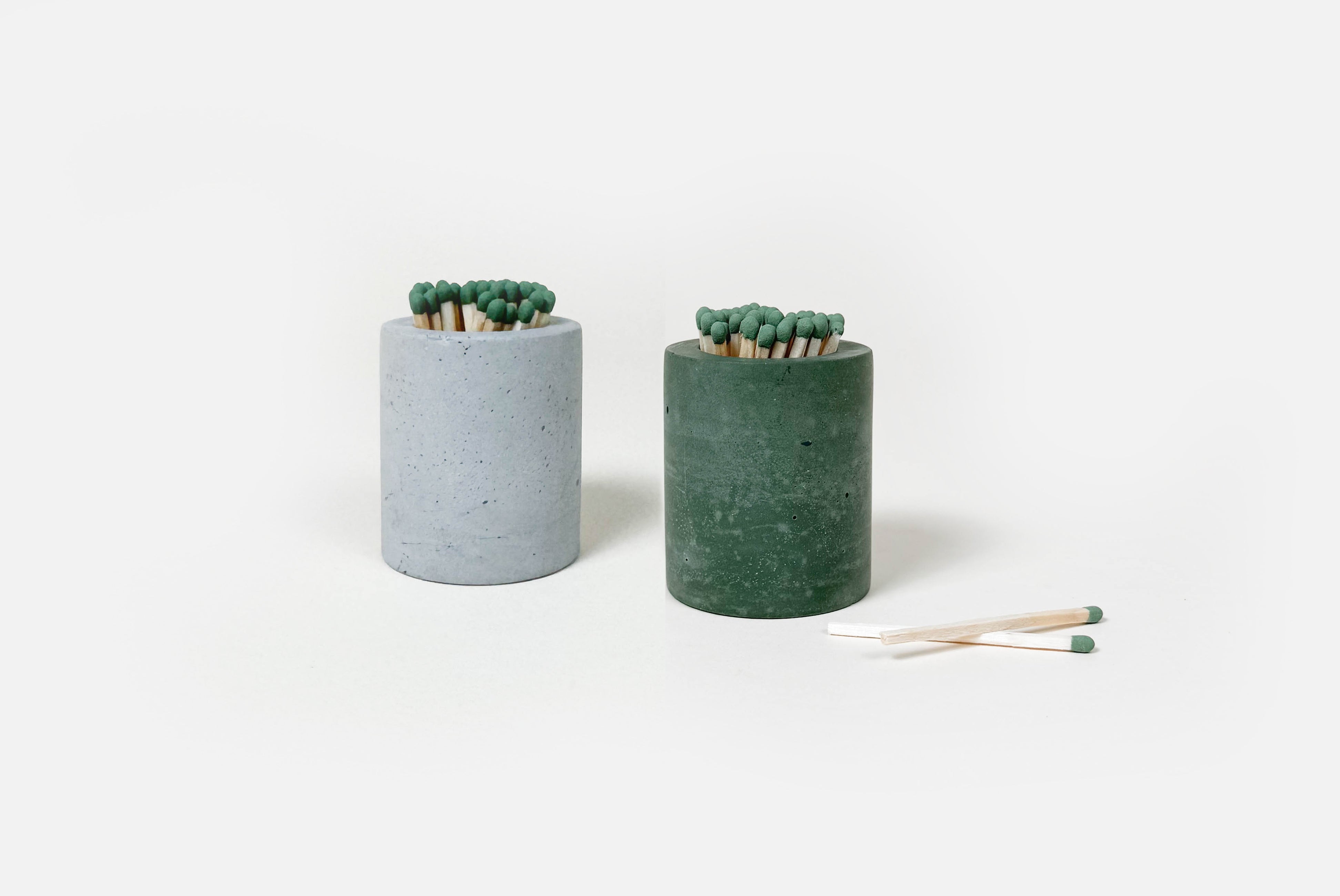 Concrete Match Holders by Linda Makess, shown in gray and green with matches, on white background