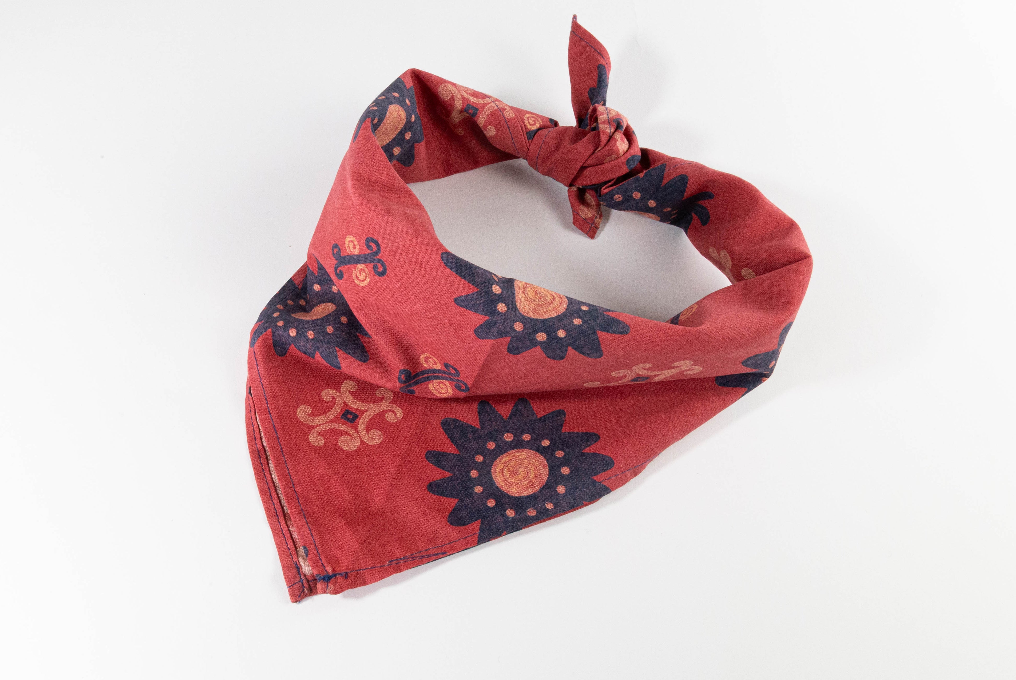 Original design red blue yellow floral print bandana. Photo of bandana tied on white background.