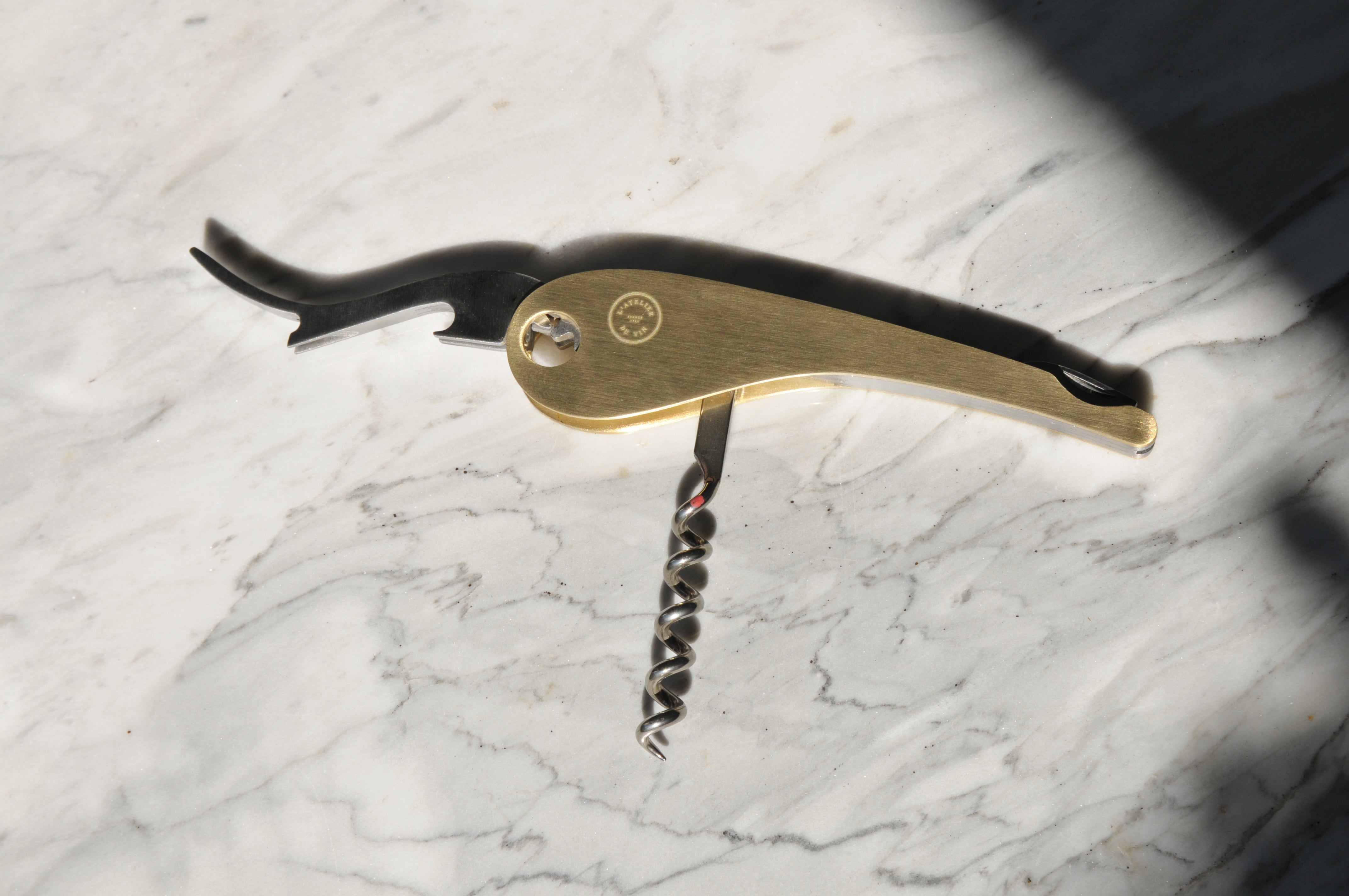 L’Atelier du Vin shown with high contrast shadows on white marble surface with bottle opener and corkscrew extended