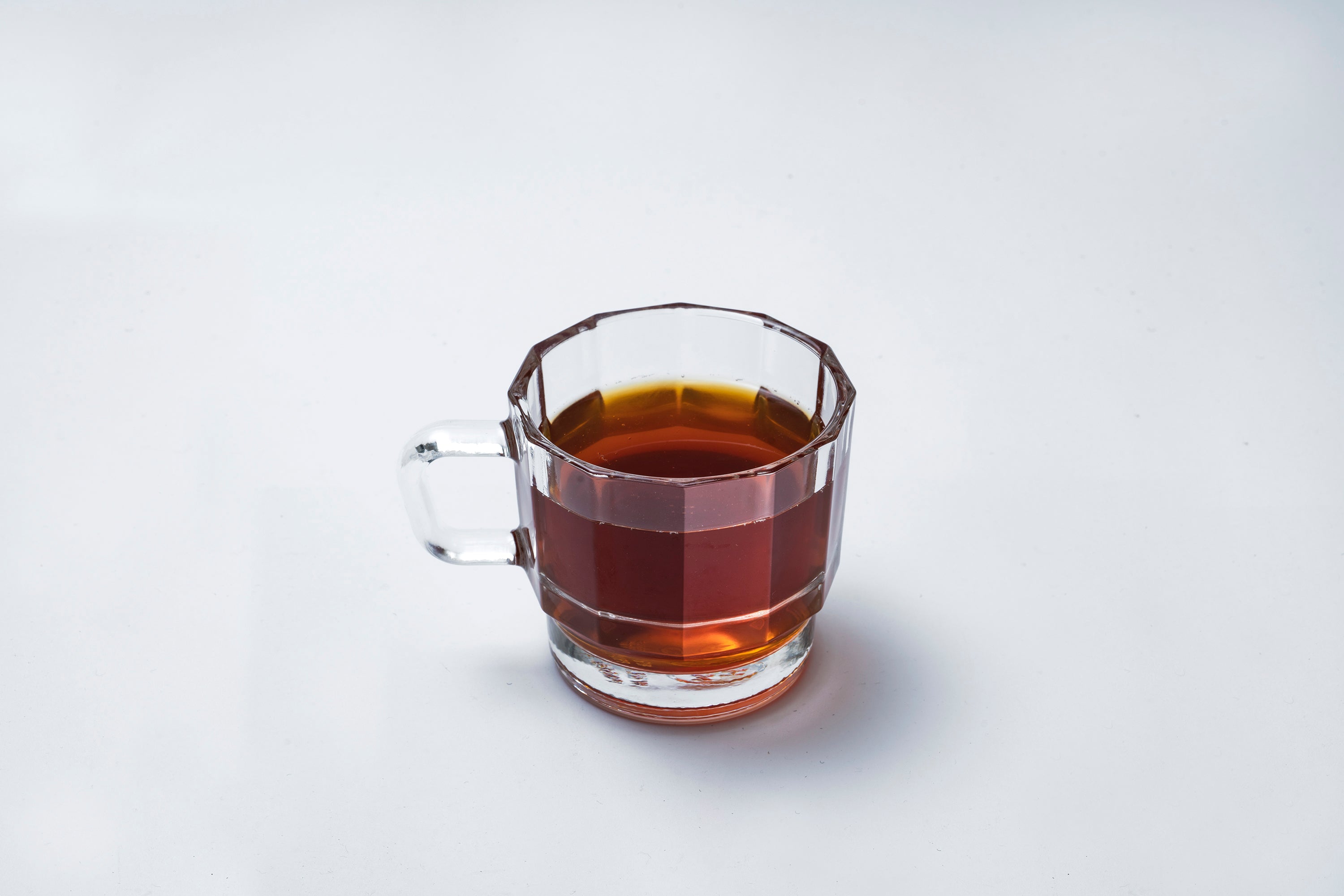 W Glass by HMM shown in clear, from side profile, filled with coffee, on white background