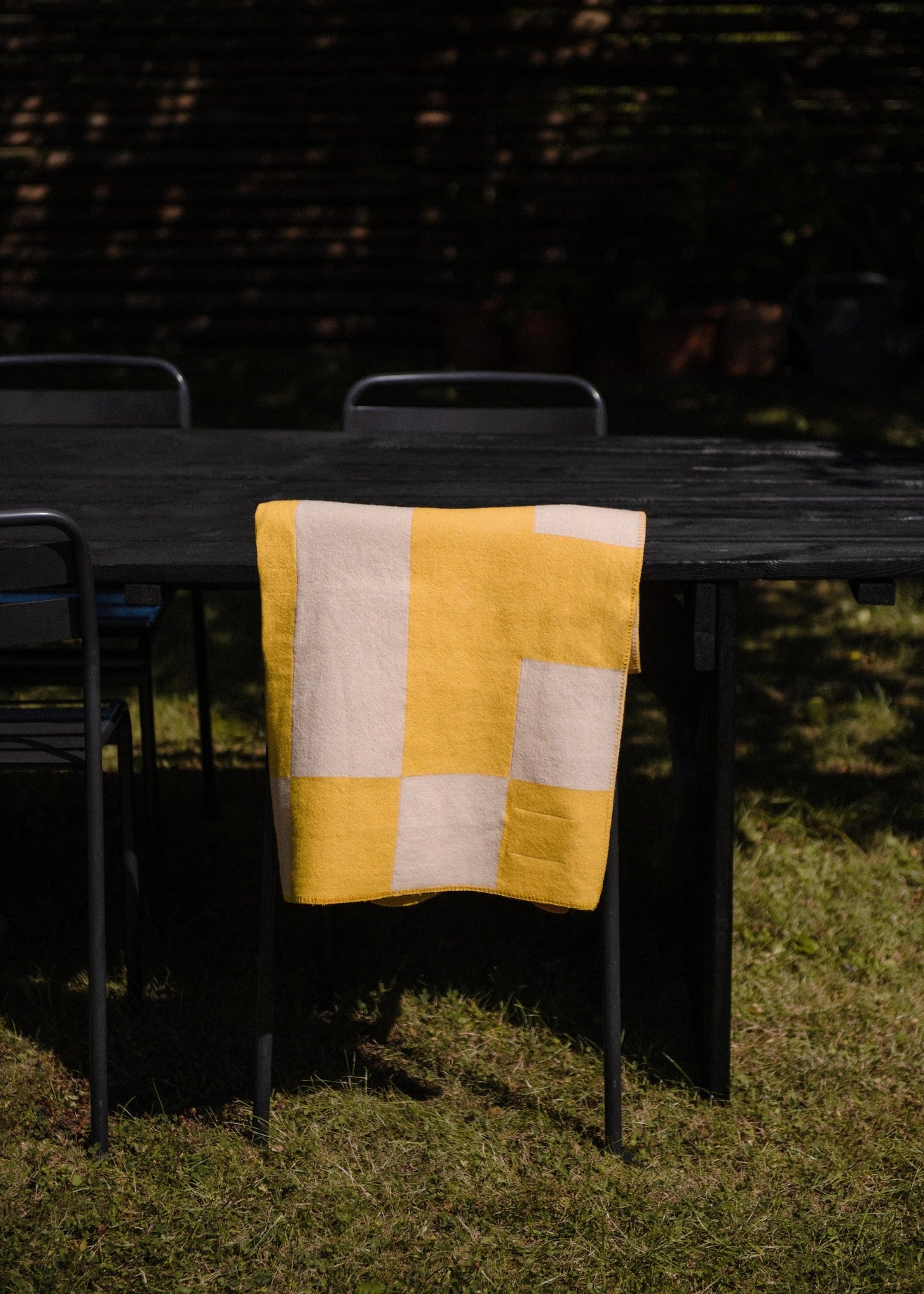 Aspen Throw Blanket in mustard shown folded and draped over the back of a chair outdoors