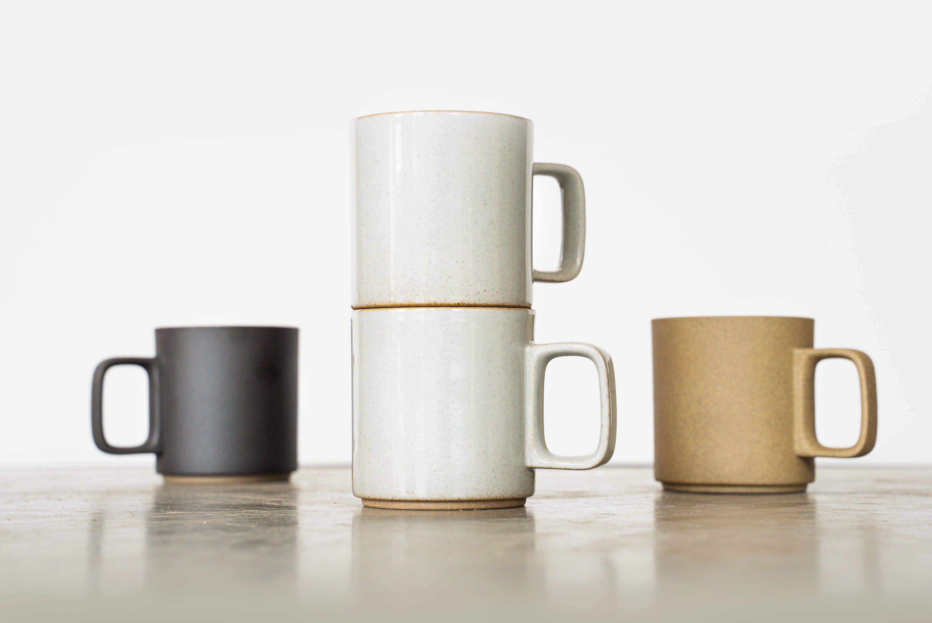 Hero shot of medium Hasami mugs with Gloss Gray stacked in front and matte black and natural set back slightly