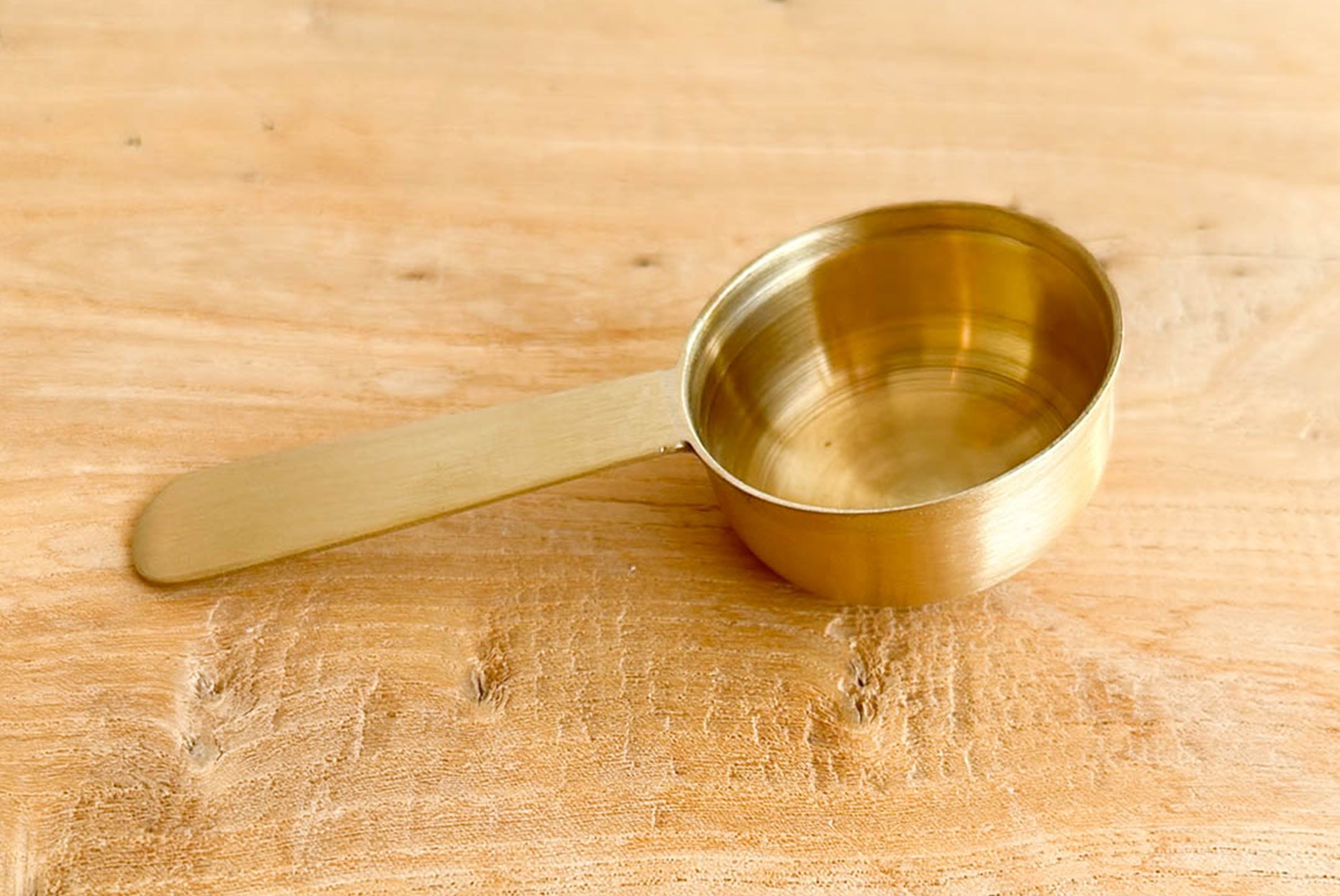 Closeup of side angle of Fog Linen Brass Scoop on wood surface