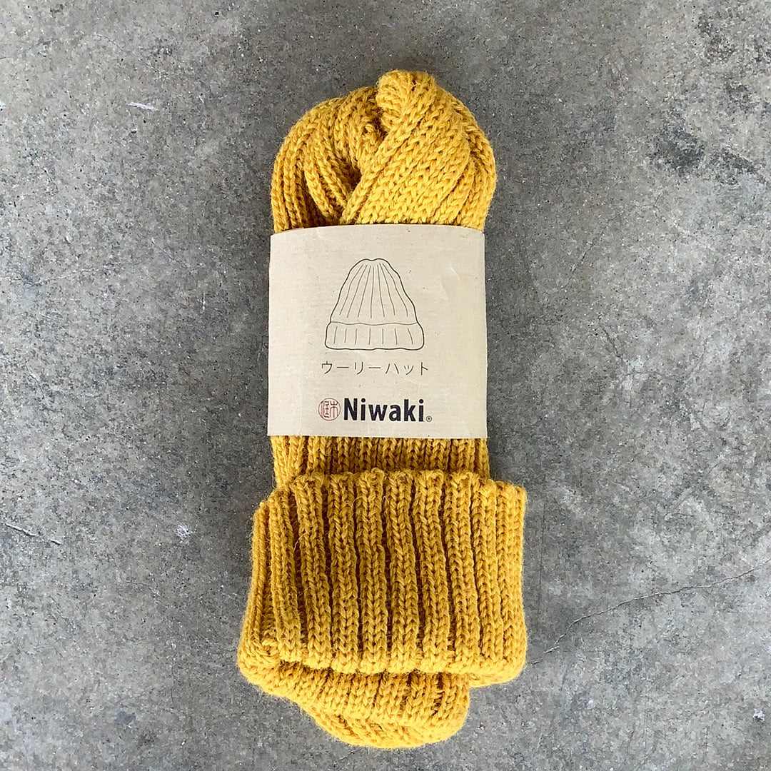 Niwaki Wool Knit Hat in mustard yellow color shown with packaging on gray background