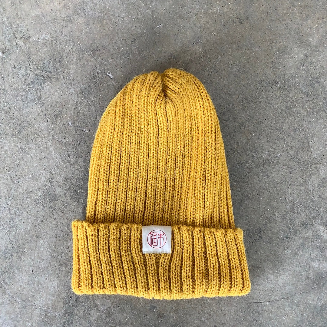 Niwaki Wool Knit Hat in yellow mustard color shown flat on gray background. Fisherman style beanie.