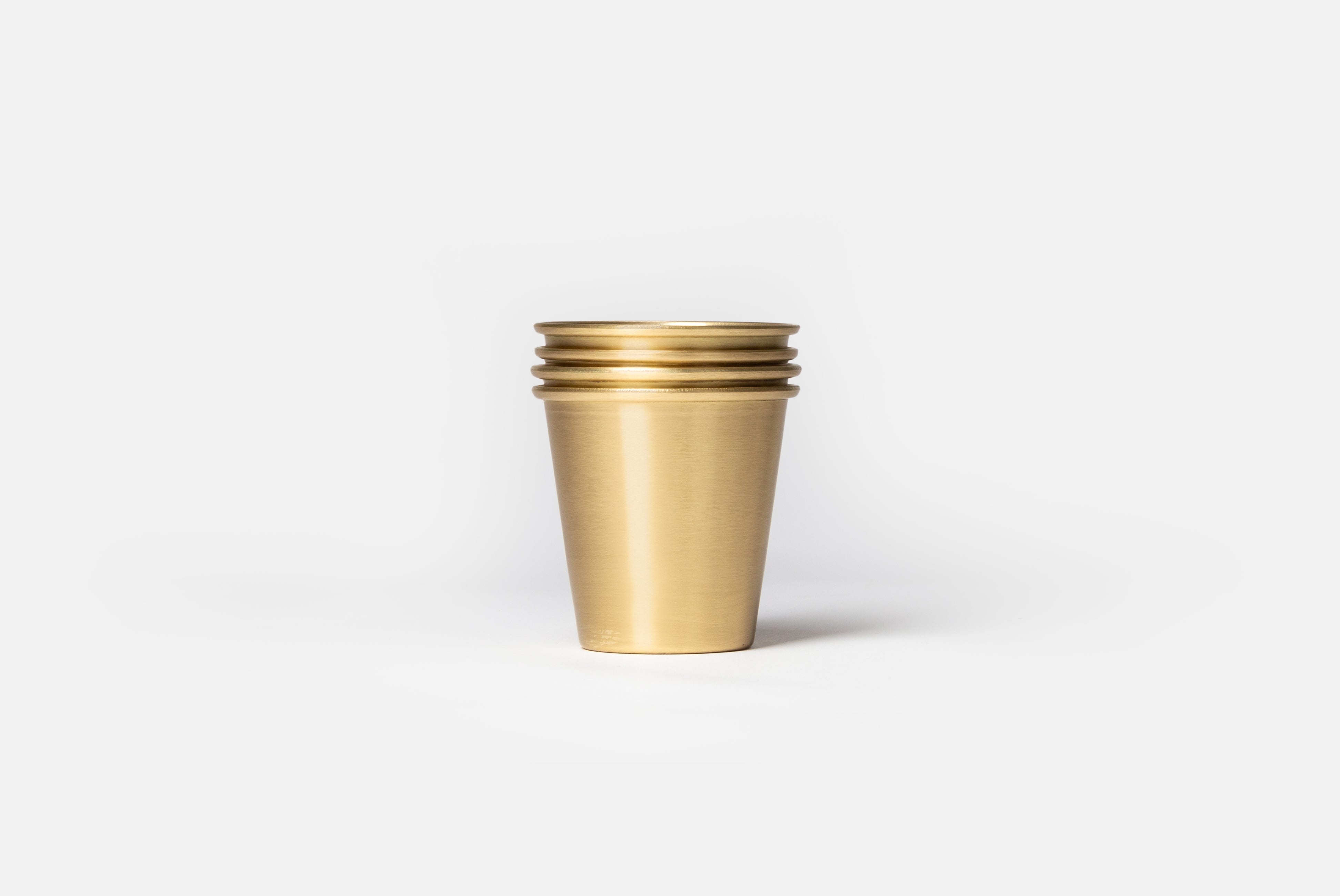 Brass Cup by Japanese Brand Fog Linen, shown in a stack of four, on a white background