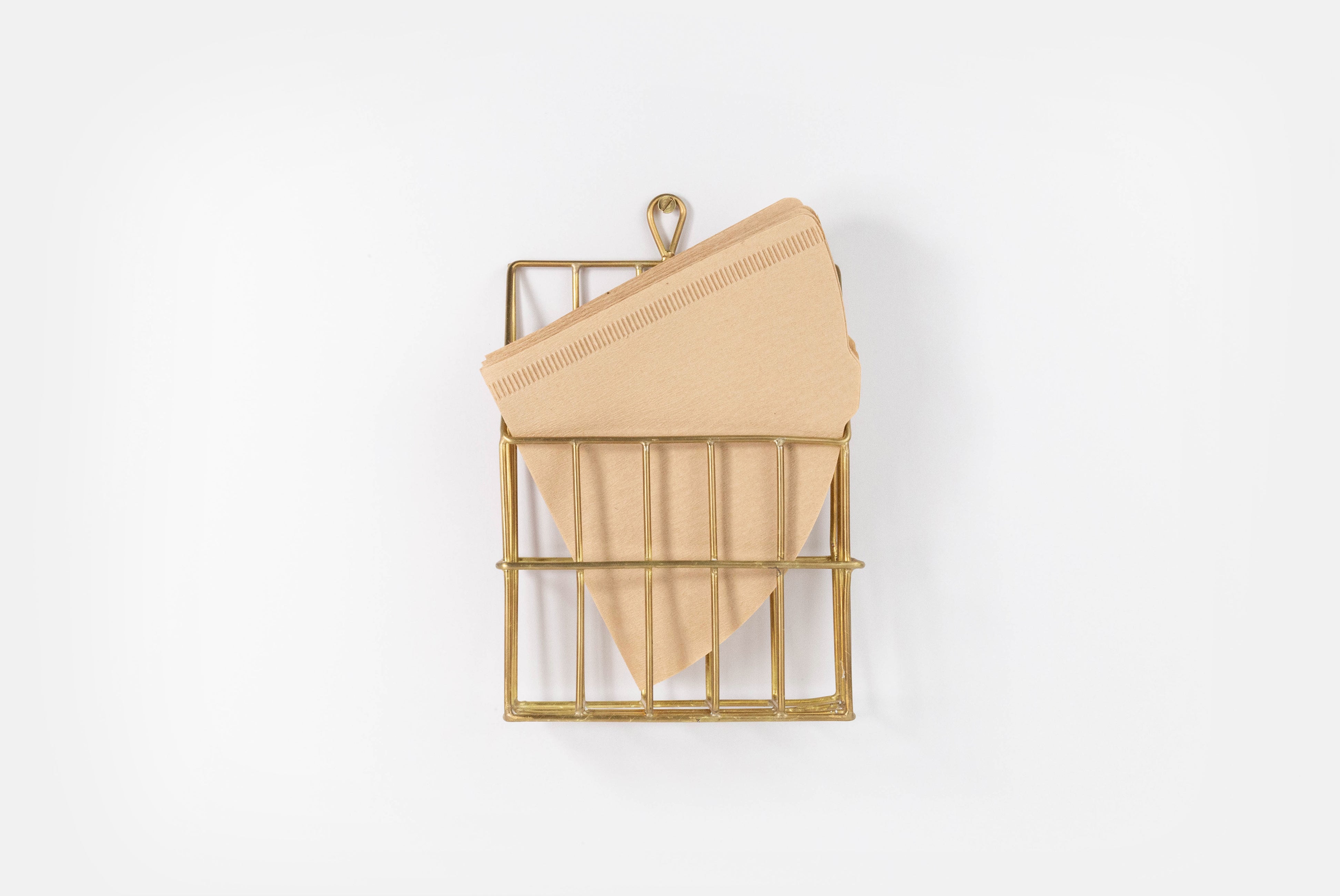 Brass Coffee Filter Holder by Fog Linen, shown hung on white background, holder filters