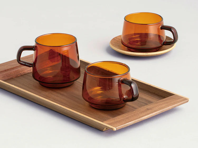 Sepia Mug by Japanese brand Kinto, shown in Amber color in two sizes with wood tray and plate