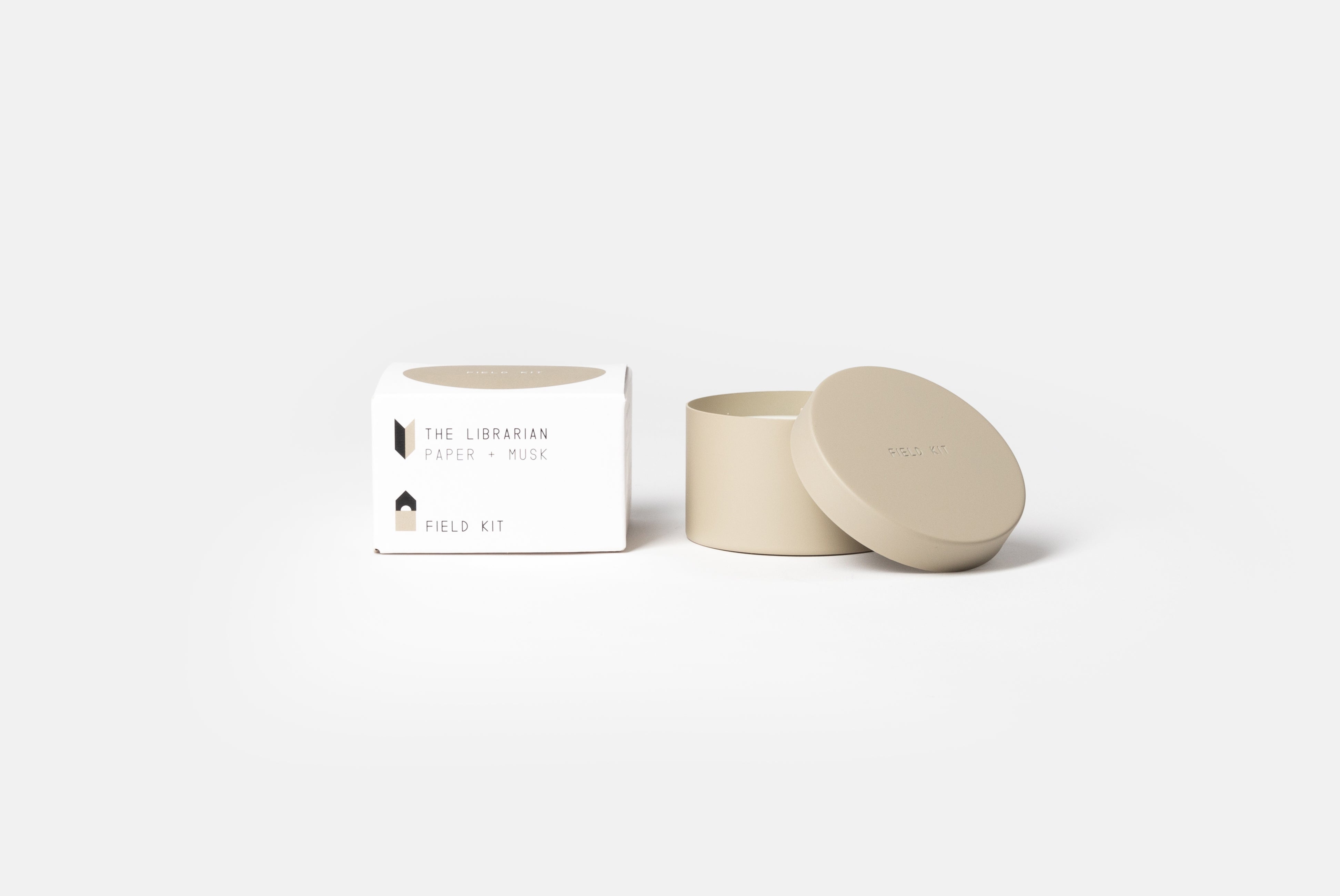 The Librarian Candle by Field Kit, shown next to packaging, with lid off, on white background